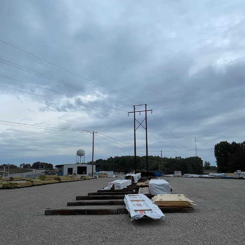 Overcast sky above a construction site with stacked materials, power lines, and a water tower in the background, conveying a calm industrial scene.