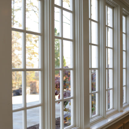 WindowsA row of tall, elegant white-framed windows with multiple panes reveals a soft, serene outdoor scene of autumn trees under gentle sunlight.